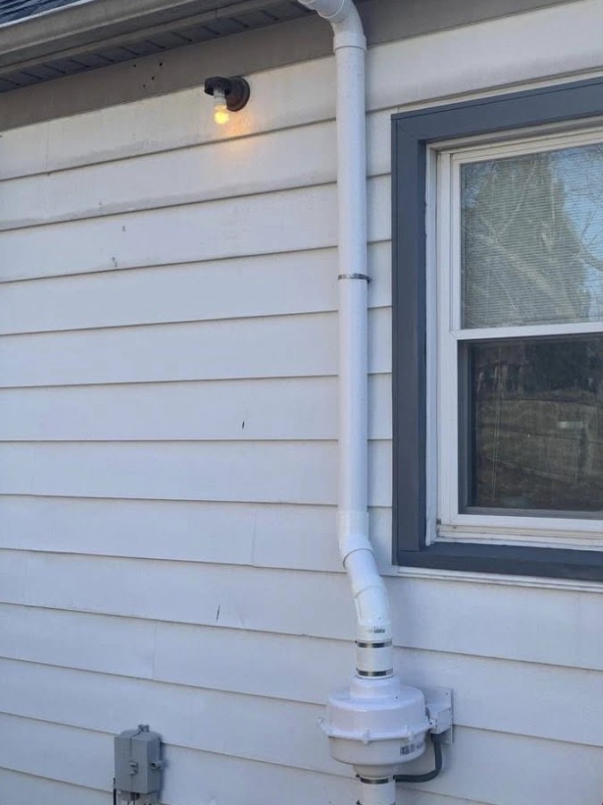 Exterior radon mitigation piping and fan installed on a home