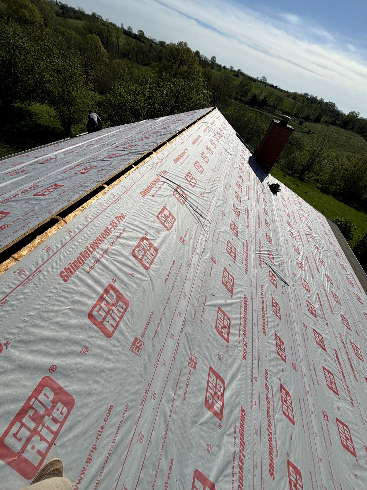 Steep farmhouse roof covered in synthetic underlayment, seen from the ridge